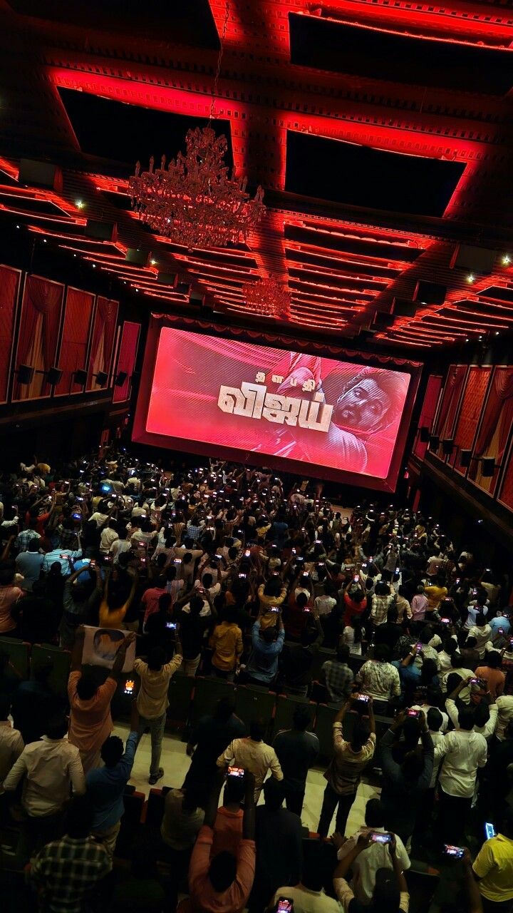 a large group of people in a room with red lighting and a big screen on the ceiling