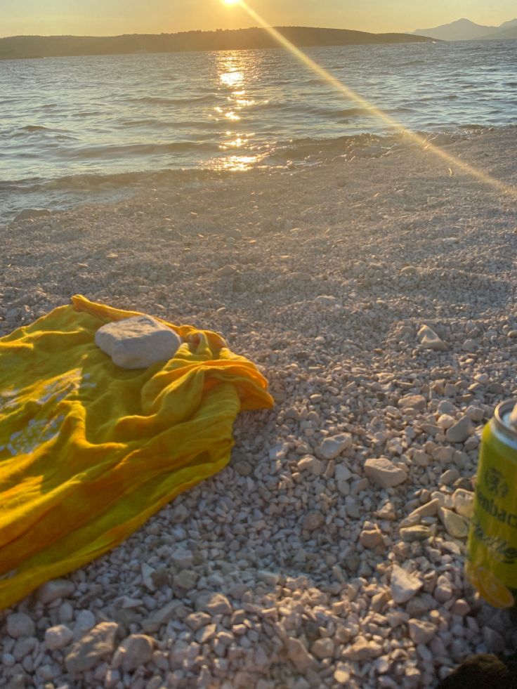 the sun is setting over the water and rocks on the beach with a yellow blanket