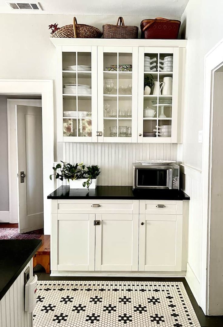 a kitchen with white cabinets and black counter tops in front of a microwave on top of a cabinet