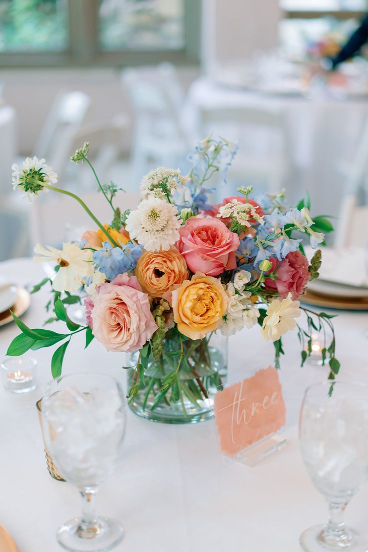 a vase filled with lots of flowers sitting on top of a table next to wine glasses