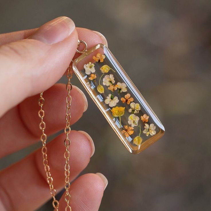 a person holding a tiny glass bottle with flowers inside it on a gold plated chain