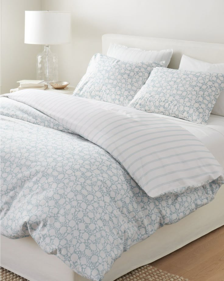 a white bed with blue and white comforter in a bedroom next to a lamp