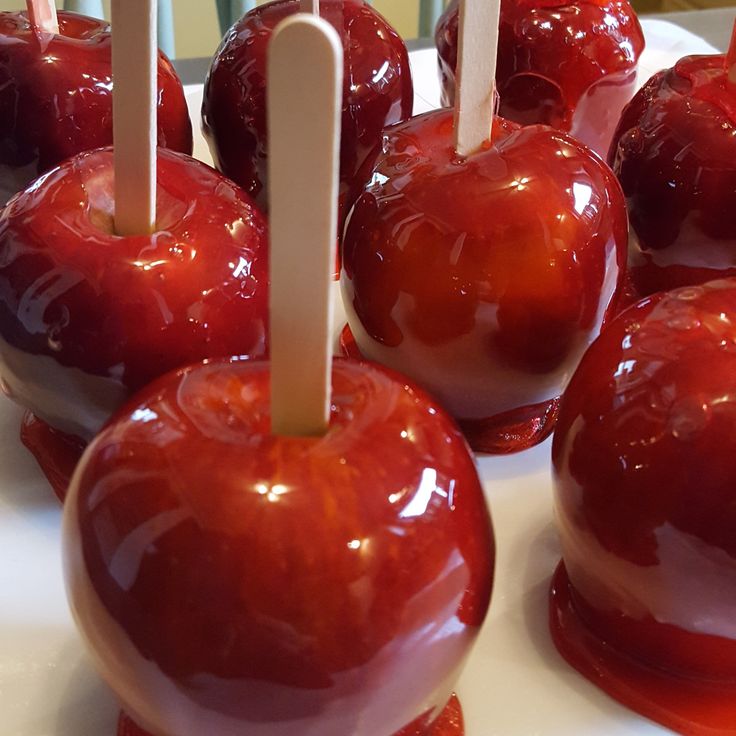 several candy apples on a white plate with toothpicks in the shape of an apple