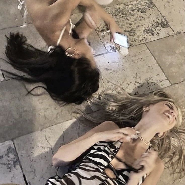 two women laying on the ground with their hair blowing in the wind