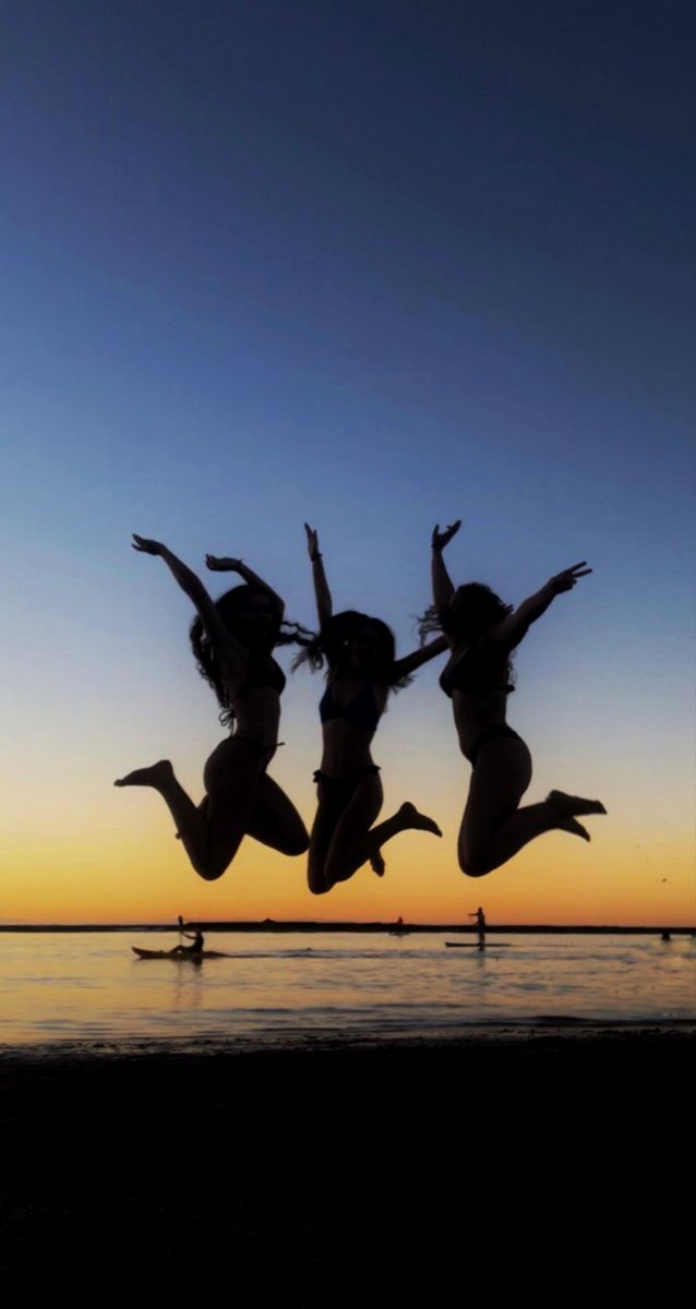 three women jumping into the air at sunset