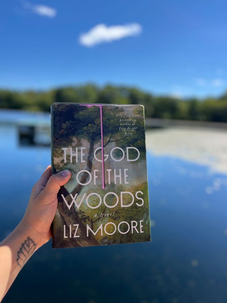 a person holding up a book about the god of the woods by liz moore