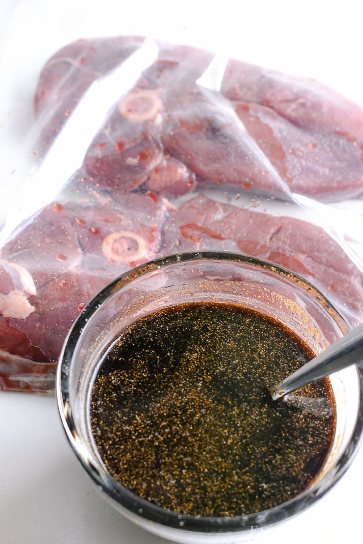 raw meat in a glass bowl with seasoning next to it on a white surface