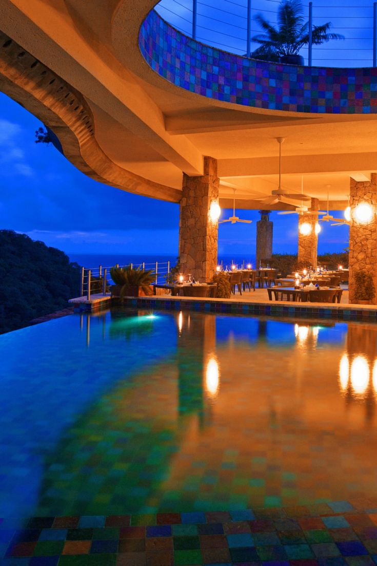 an indoor swimming pool at night with lights on the ceiling and large windows above it