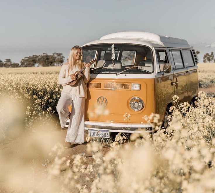 a woman standing next to an old vw bus in a field full of wildflowers