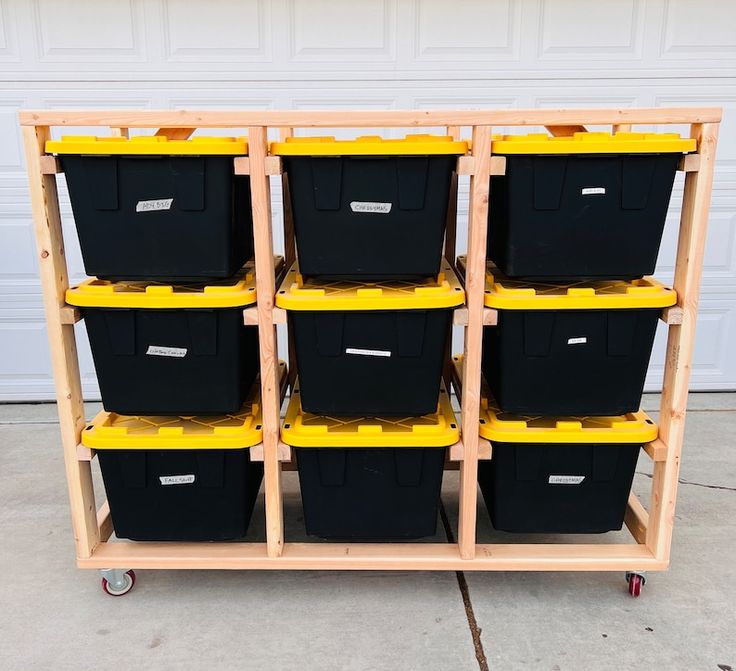 several black and yellow bins are stacked on a wooden cart with wheels in front of a garage door