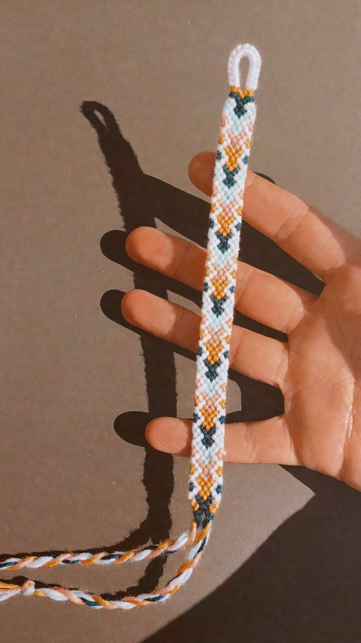 a hand is holding a string that looks like a cross stitch bracelet