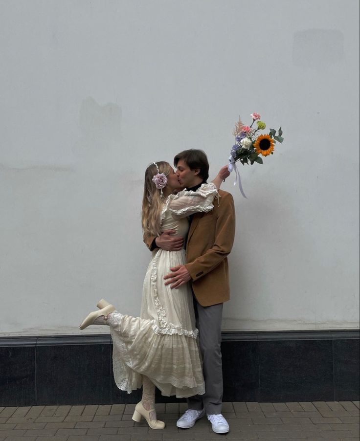 a man and woman kissing in front of a white wall with sunflowers on it