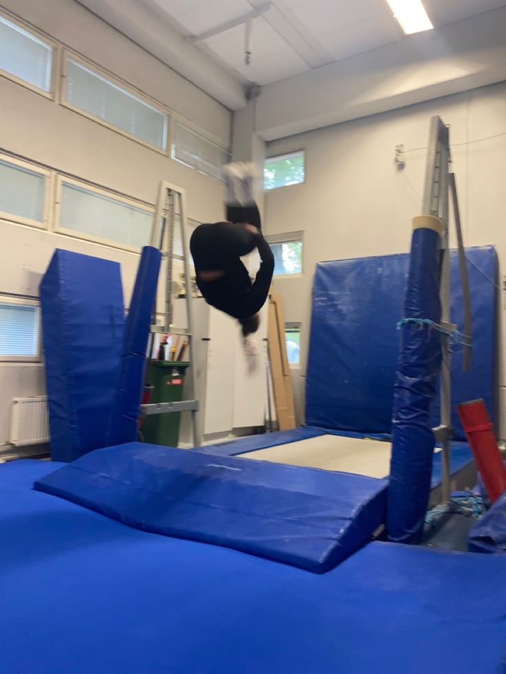 a person jumping on a trampoline in an indoor area with blue tarps