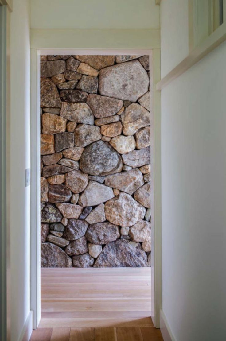 an open door leading to a stone wall and hardwood floored hallway with hard wood floors