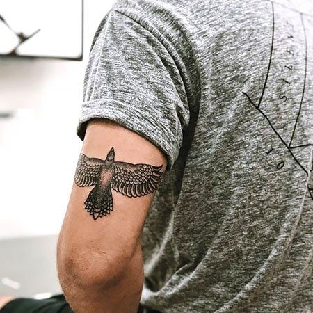 a man with a black bird tattoo on his arm sitting in front of a white wall