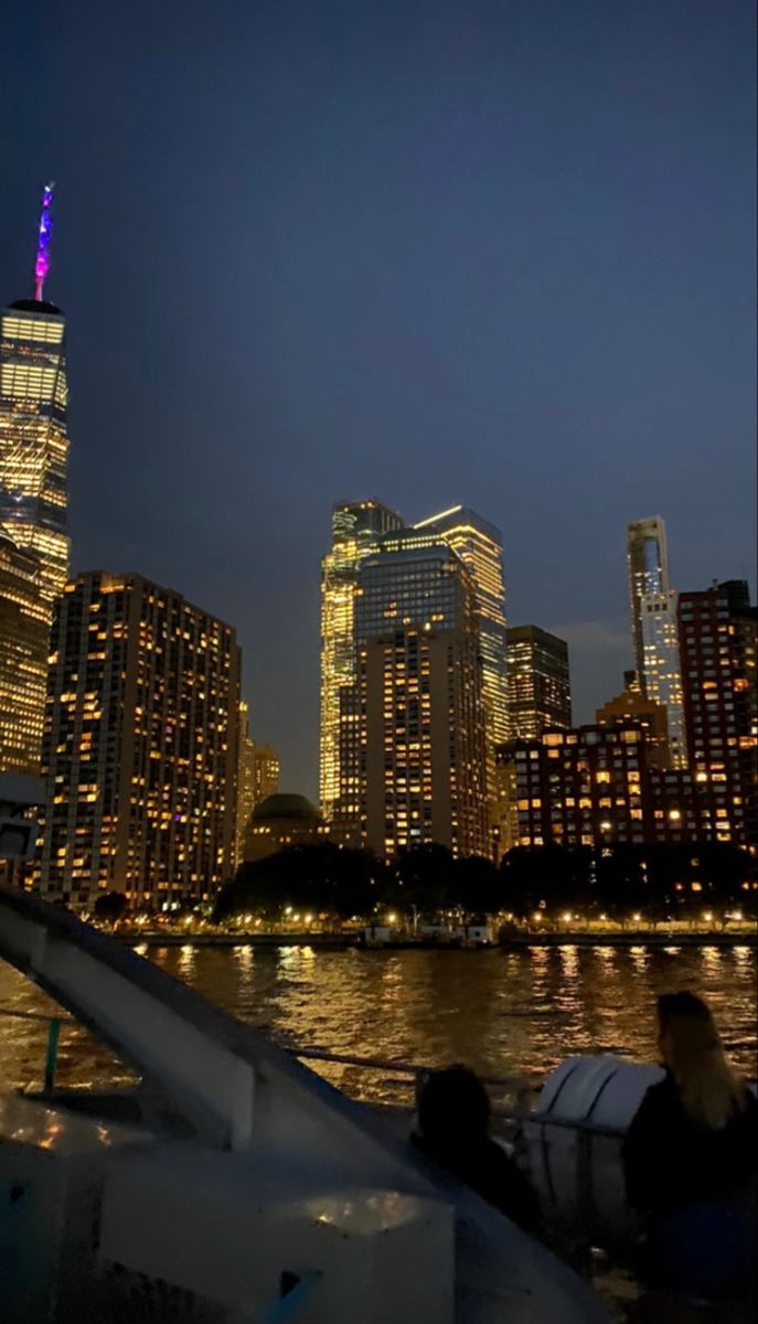 the city skyline is lit up at night as people sit on a boat in the water