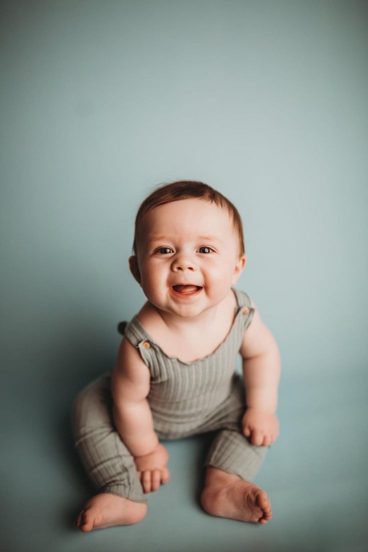 a smiling baby sitting on the floor in front of a blue wall and looking at the camera