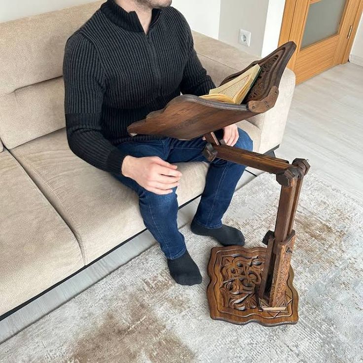 a man sitting on top of a couch next to a wooden book holder with an open book in it