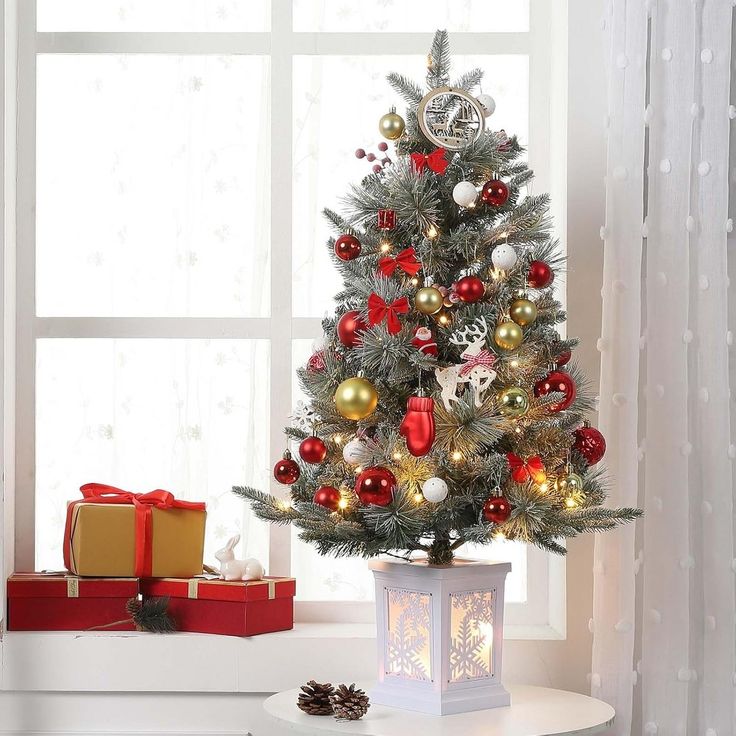 a small christmas tree with red, gold and silver ornaments in a living room window sill