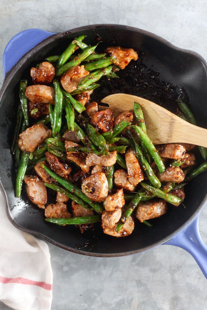 a skillet with chicken and green beans on the side, next to a wooden spoon