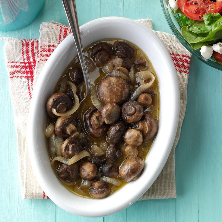 a white bowl filled with mushrooms and onions next to a salad on top of a blue table