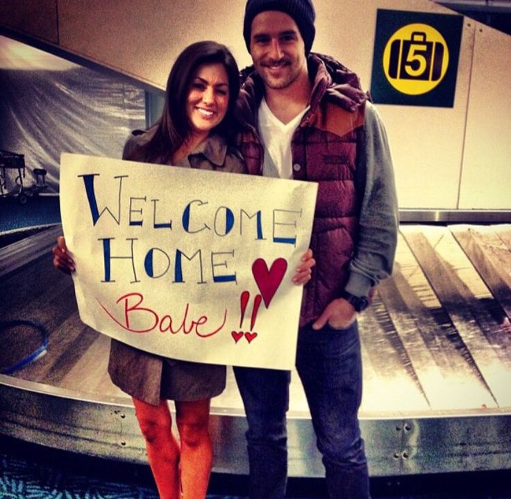 a man and woman standing next to each other holding a sign that says welcome home babe