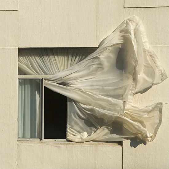 an open window covered in white fabric next to a curtain on the side of a building