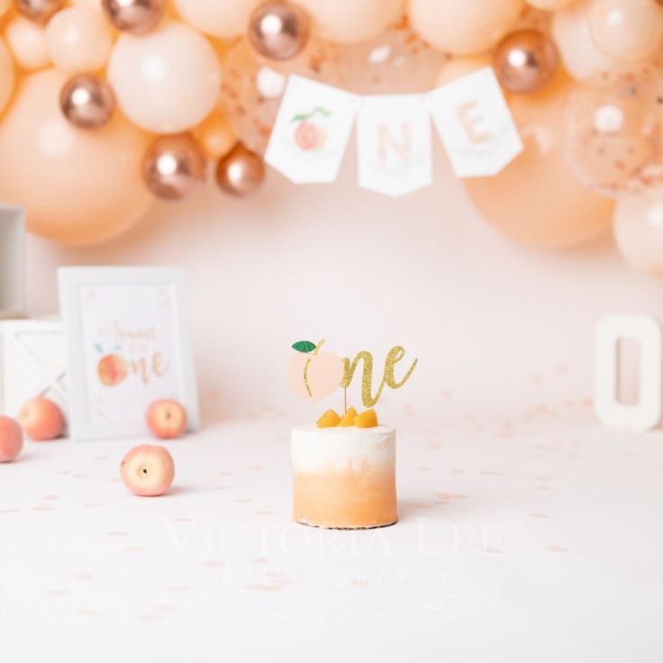 a cake with the number one on it sits in front of balloons and decorations for an apple themed first birthday party