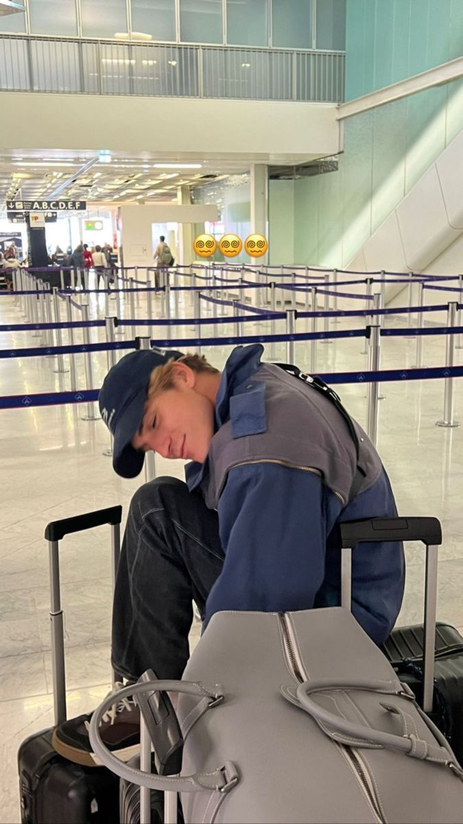 a man sitting in an airport with his head down and luggage on the ground next to him