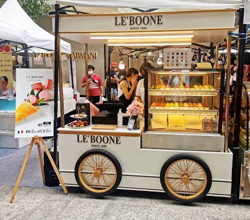 an ice cream cart with people standing at the front and behind it, selling food