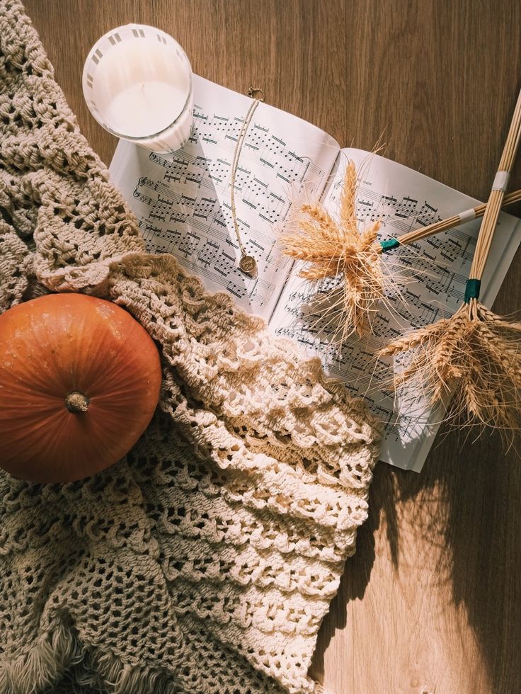 an open book with yarn and pumpkins next to it on top of a wooden table