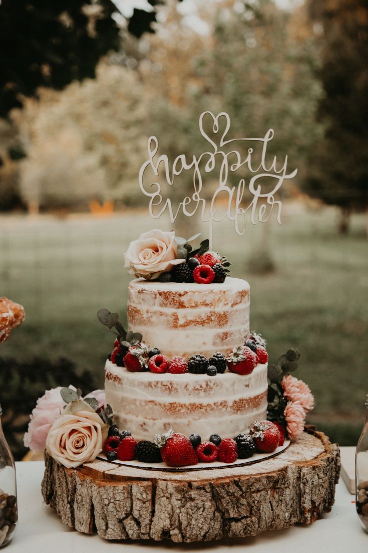 a wedding cake sitting on top of a tree stump with berries and flowers around it