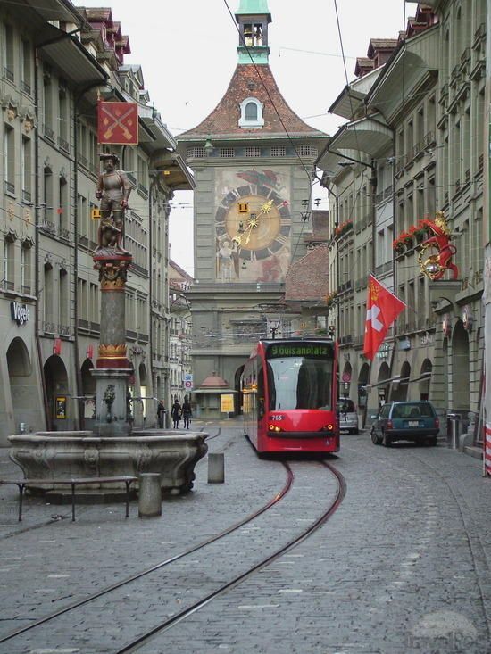 a red train is going down the tracks in an old european city with tall buildings