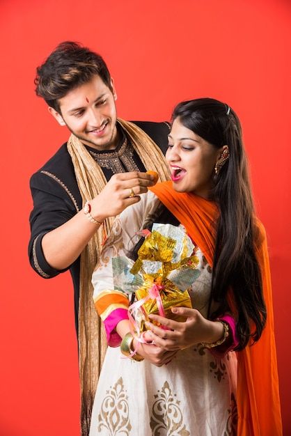 a man and woman standing next to each other in front of a red wall eating food