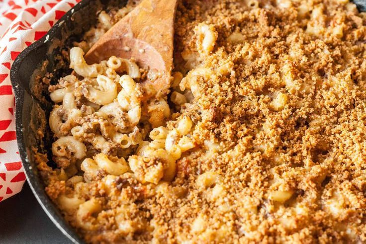 a skillet filled with macaroni and cheese on top of a red checkered cloth