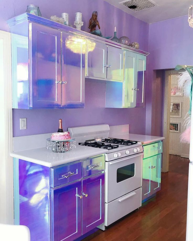 a kitchen with purple walls and white cabinets, an oven and sink are in the center of the room