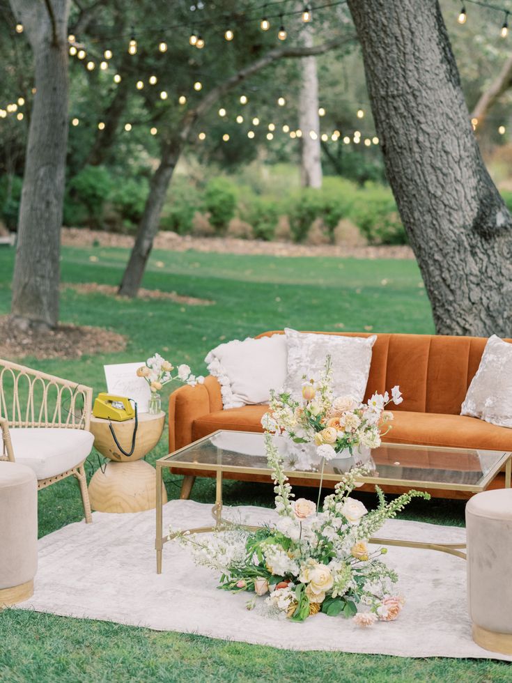 a living room filled with furniture and flowers on top of a white rug in front of a tree