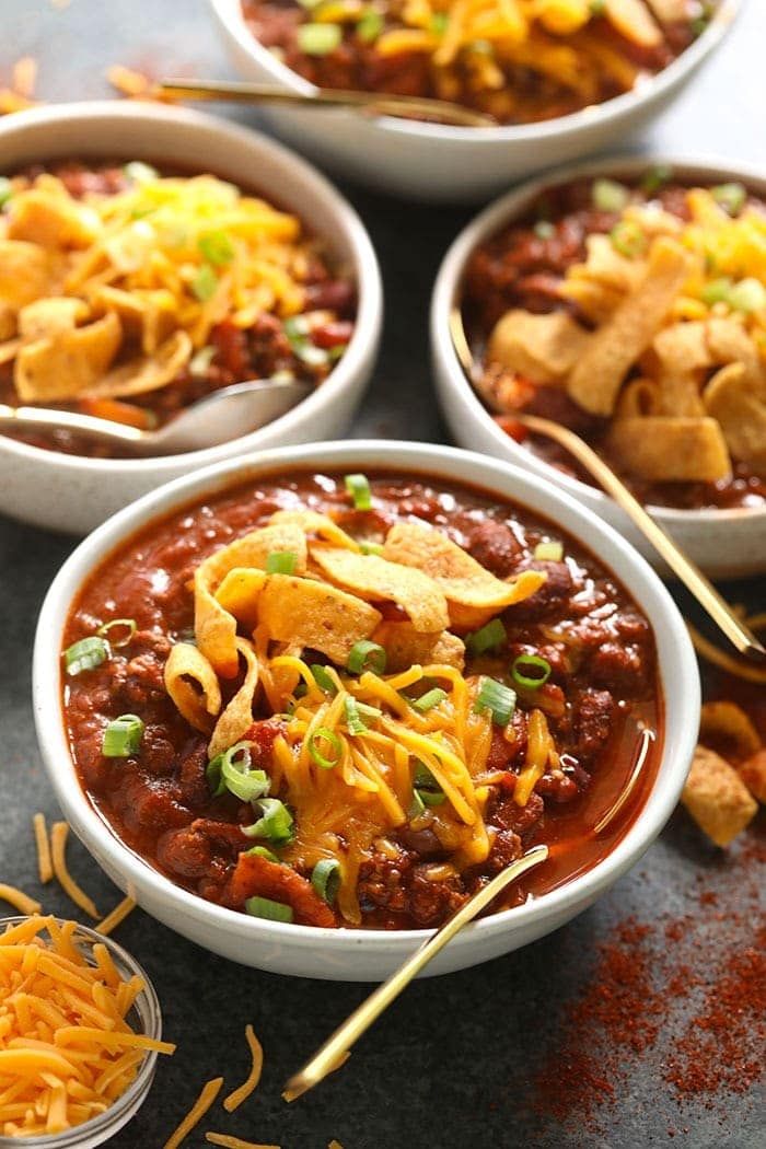 four bowls filled with chili, cheese and tortilla chips on top of a table