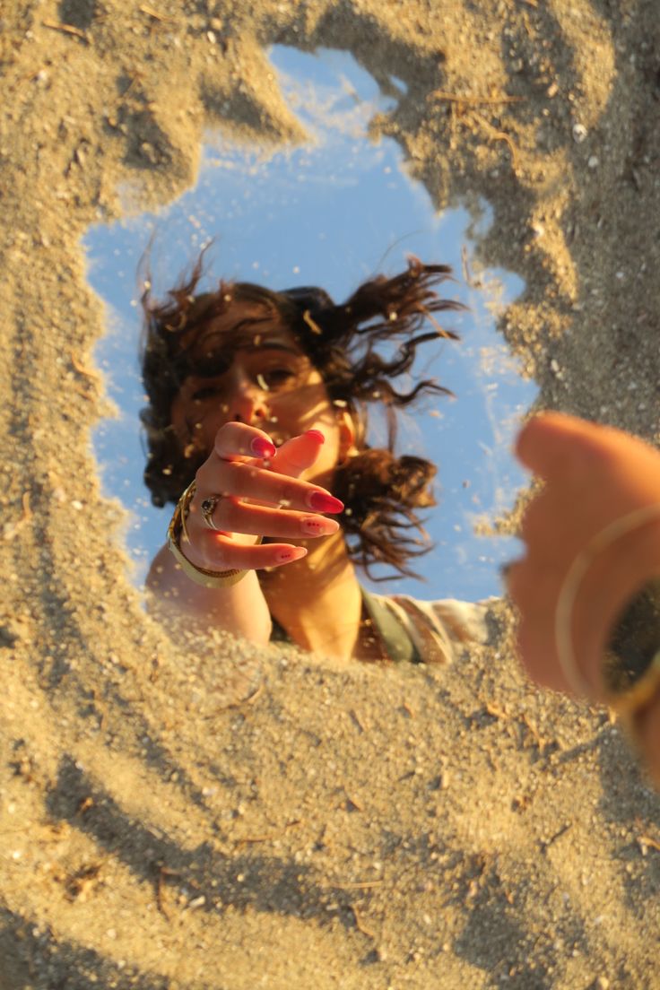 a woman taking a selfie in the sand with her hand out to take a photo