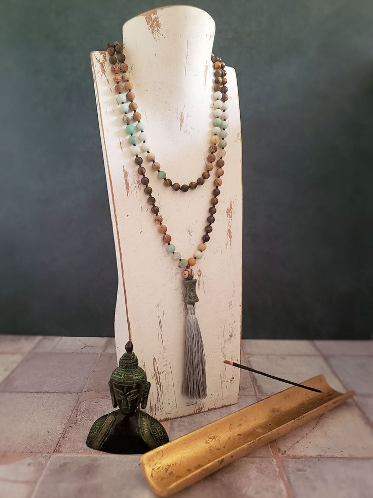 This beautiful Mala Necklace is made with 108 beads of Amazonite, Tiger's Eye, and Picture Jasper, each with its own unique healing properties. The Accent Dzi beads are believed to have protective and healing properties. This Mala necklace is not only a stunning accessory but also a tool for meditation and mindfulness. The necklace is hand-knotted between each bead and finished with a tassel under the Dzi beads.Materials & style:- 108 beads for traditional Mala use- Dzi beads for spiritual signi Spiritual Amazonite 8mm Beads Jewelry, Spiritual Amazonite Jewelry With 8mm Beads, Spiritual Round Beads Crystal Necklaces For Layering, Spiritual Crystal Necklaces With Round Beads For Layering, Spiritual Round Beads Necklaces For Layering, Handmade Spiritual Necklace For Layering, Holistic Crystal Necklaces With 8mm Beads For Meditation, Holistic Crystal Necklace With 8mm Beads For Meditation, Holistic Crystal Necklace For Meditation With 8mm Beads