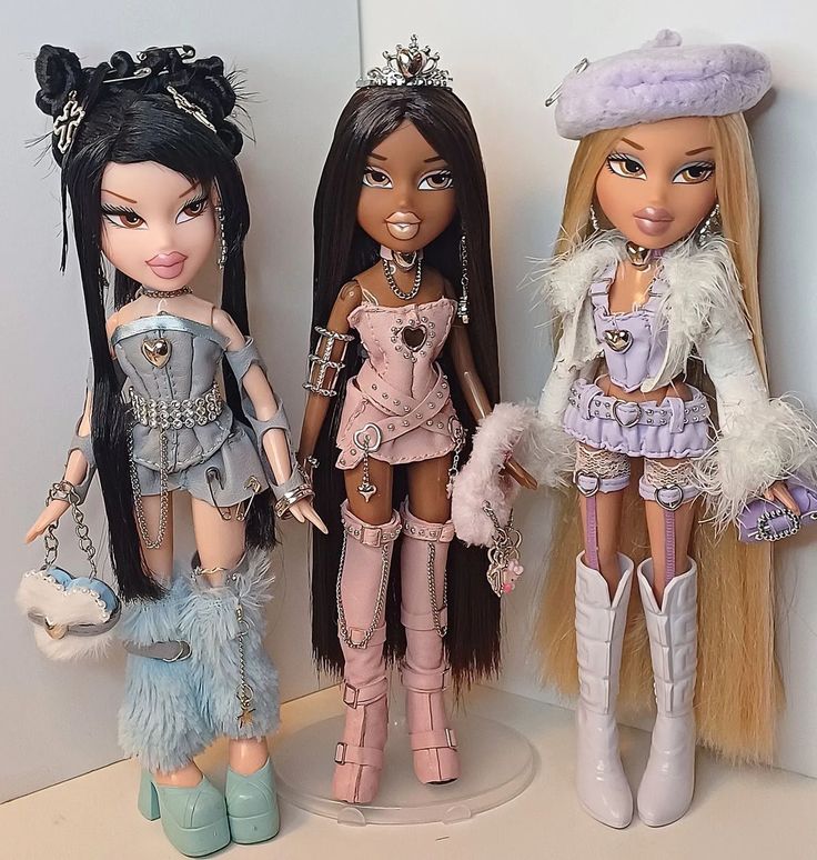 three dolls standing next to each other in front of a white wall and two are holding purses