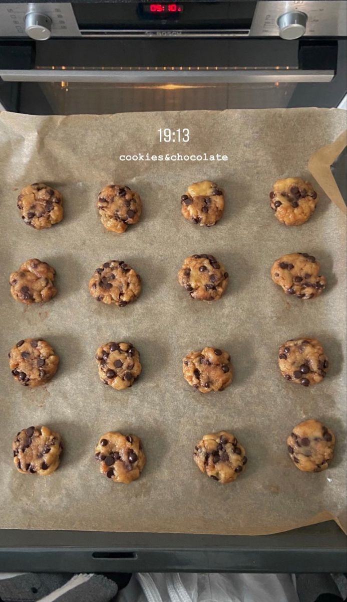 chocolate chip cookies are lined up on a sheet of parchment paper in front of an oven