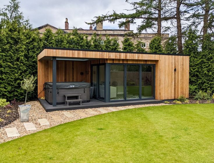 a small wooden building sitting in the middle of a lush green yard with an outside hot tub