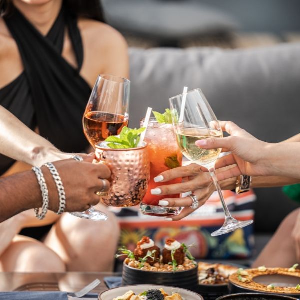 people are toasting with glasses of wine and food on a table in front of them