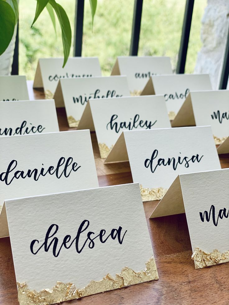 place cards with names on them sitting on a table next to a potted plant