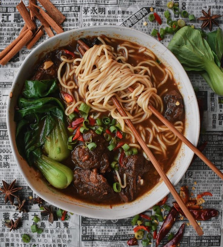 a bowl filled with noodles, meat and veggies on top of a newspaper