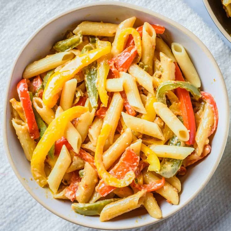 a bowl filled with pasta and vegetables on top of a white cloth next to a fork