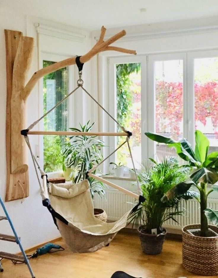 a hammock hanging from a tree branch in a room with potted plants