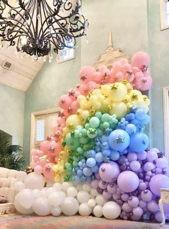 a rainbow balloon arch in a room with chandelier