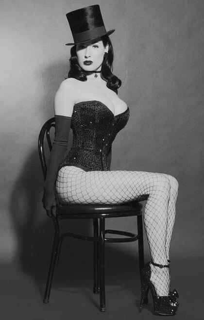 a woman sitting on top of a chair wearing fishnet stockings and a top hat